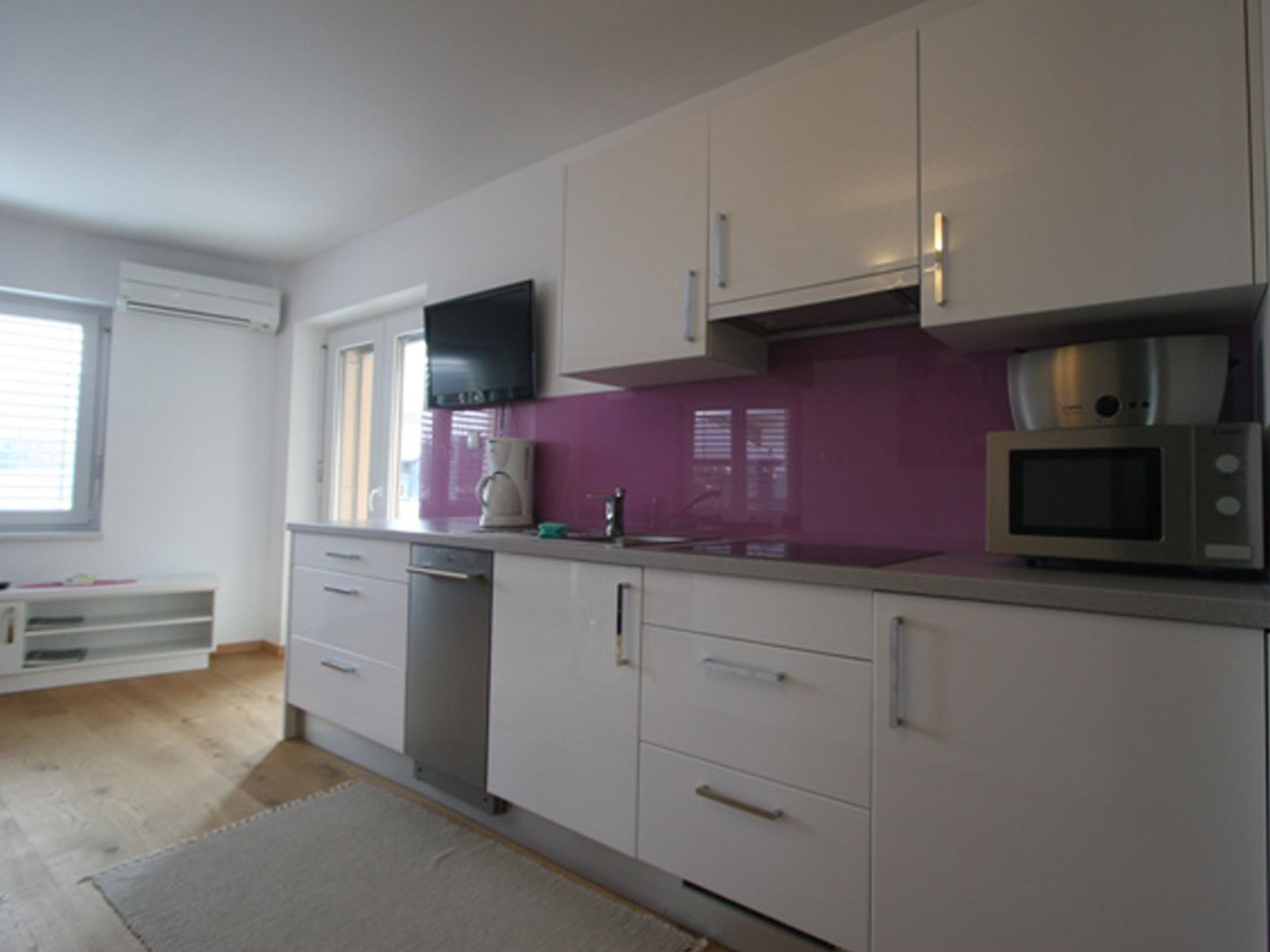 A modern kitchen with white cabinets, a purple backsplash, a microwave, and a coffee maker.