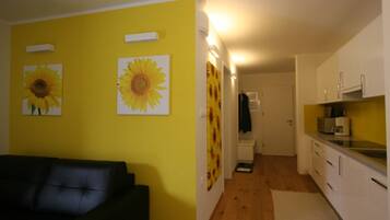 A room with a black sofa, a kitchen with white cabinets, and sunflower artwork on the walls.