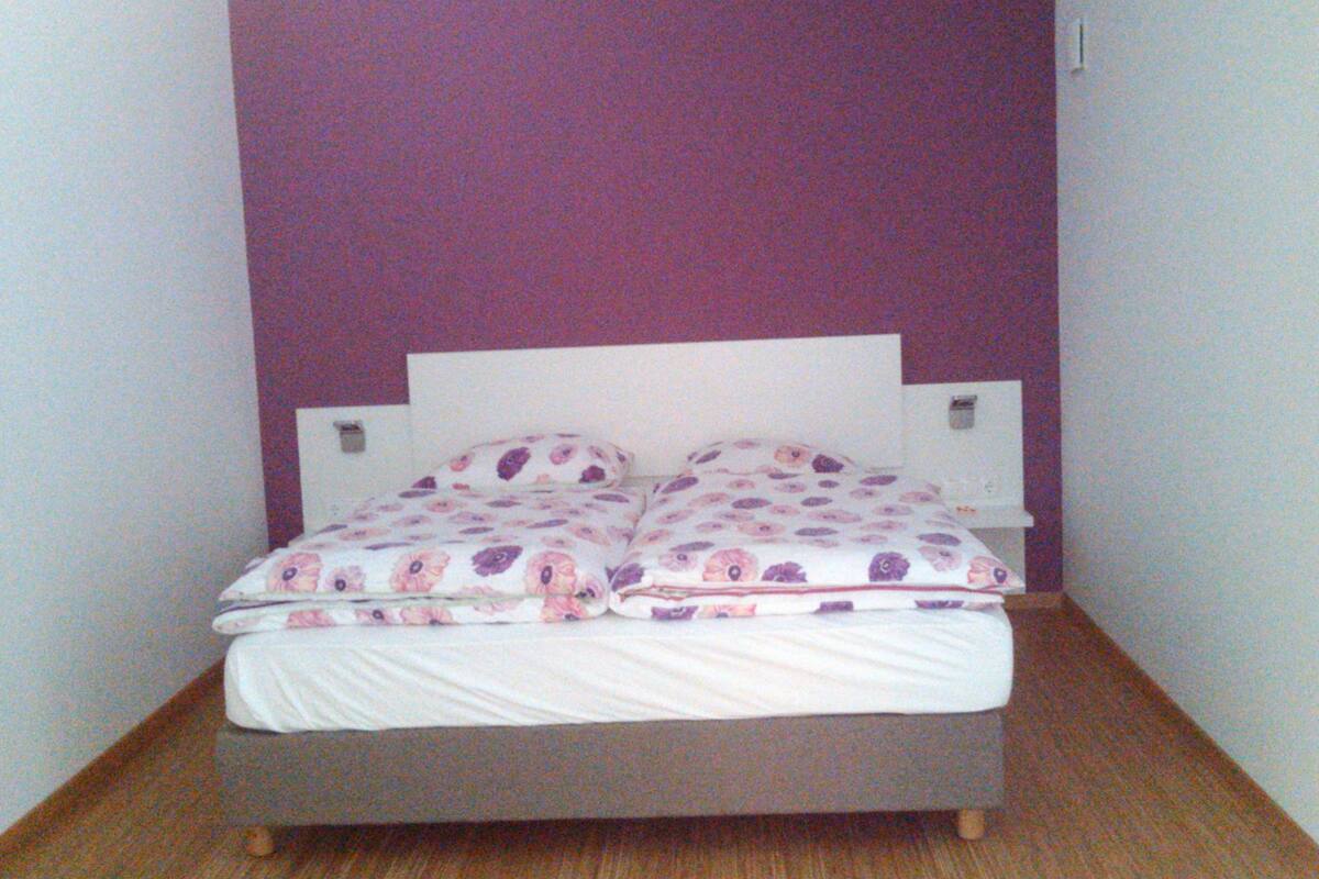 Een eenpersoonsbed met een bloemenprint dekbed in een kamer met paarse wanden en een wit hoofdbord.