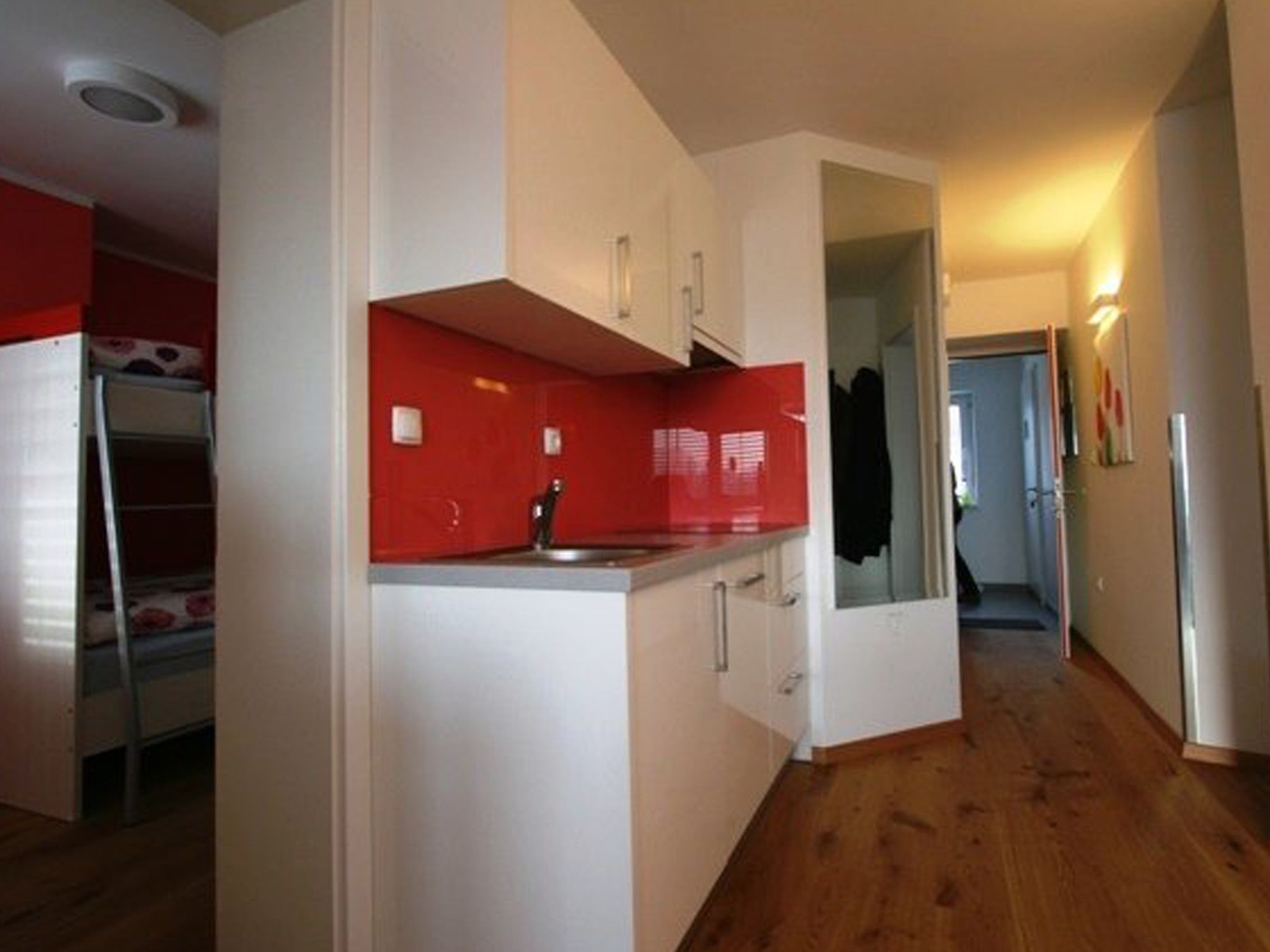 A compact kitchen with white cabinets, a red backsplash, and a wooden floor.