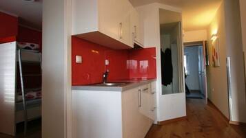 A compact kitchen with white cabinets, a red backsplash, and a wooden floor.