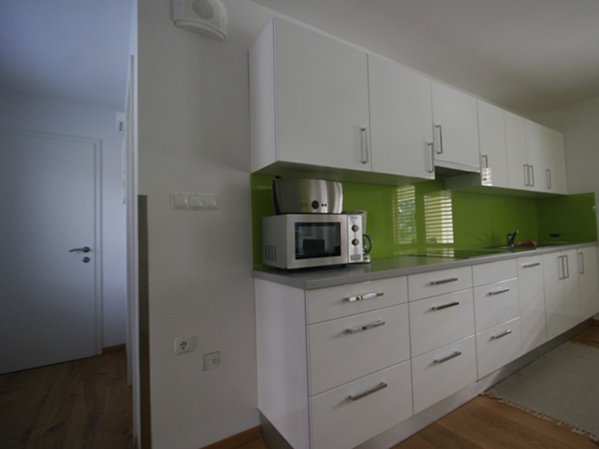 A kitchen with white cabinets, a microwave, and a green backsplash.