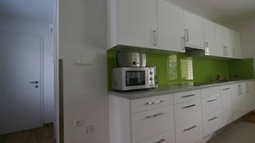 A kitchen with white cabinets, a microwave, and a green backsplash.
