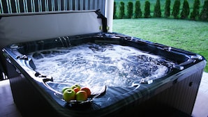 A hot tub with a glass top, surrounded by a wooden deck, and a grassy yard in the background.