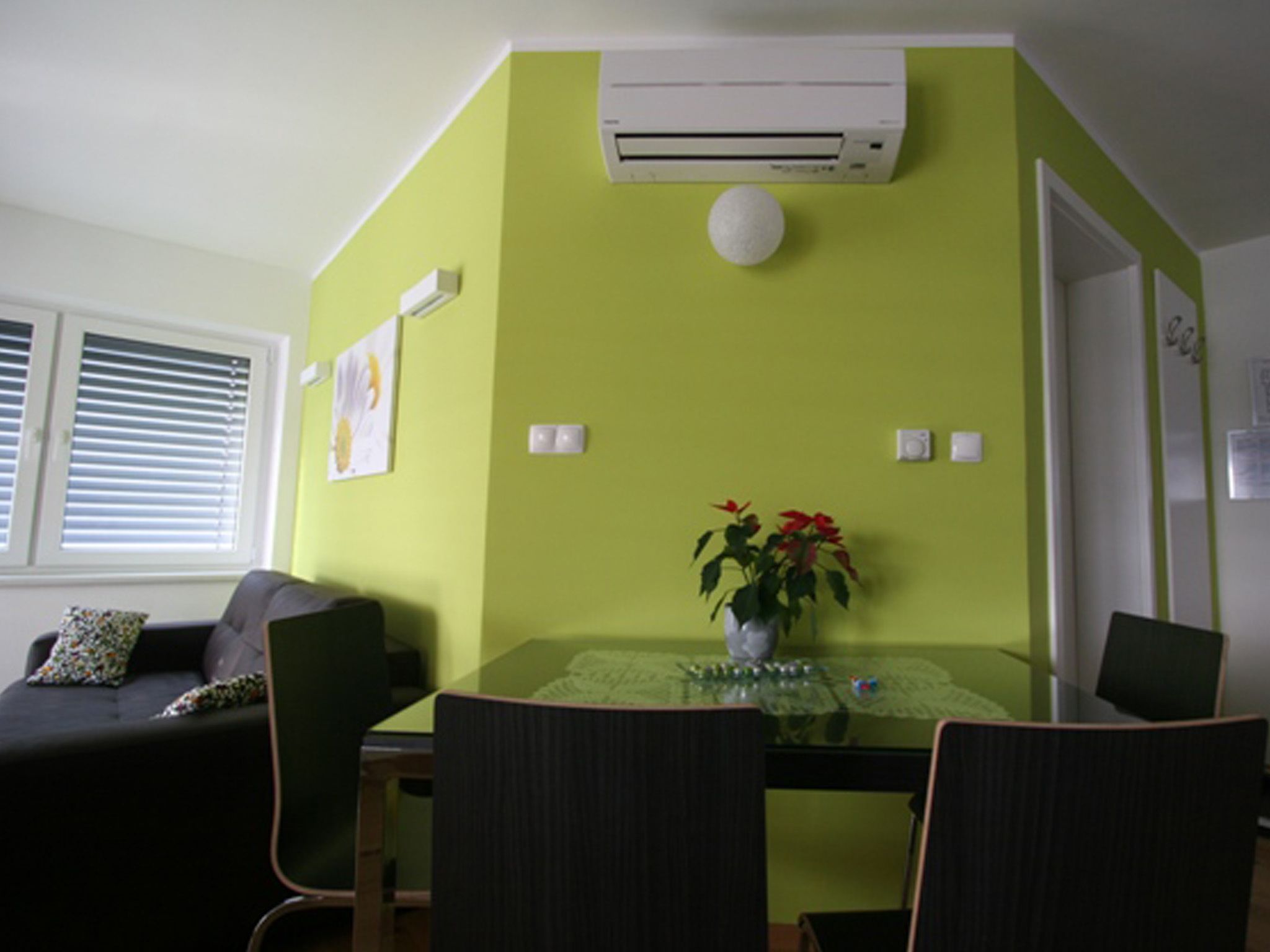 A dining area with a glass table, chairs, a vase with flowers, and an air conditioning unit on the wall.