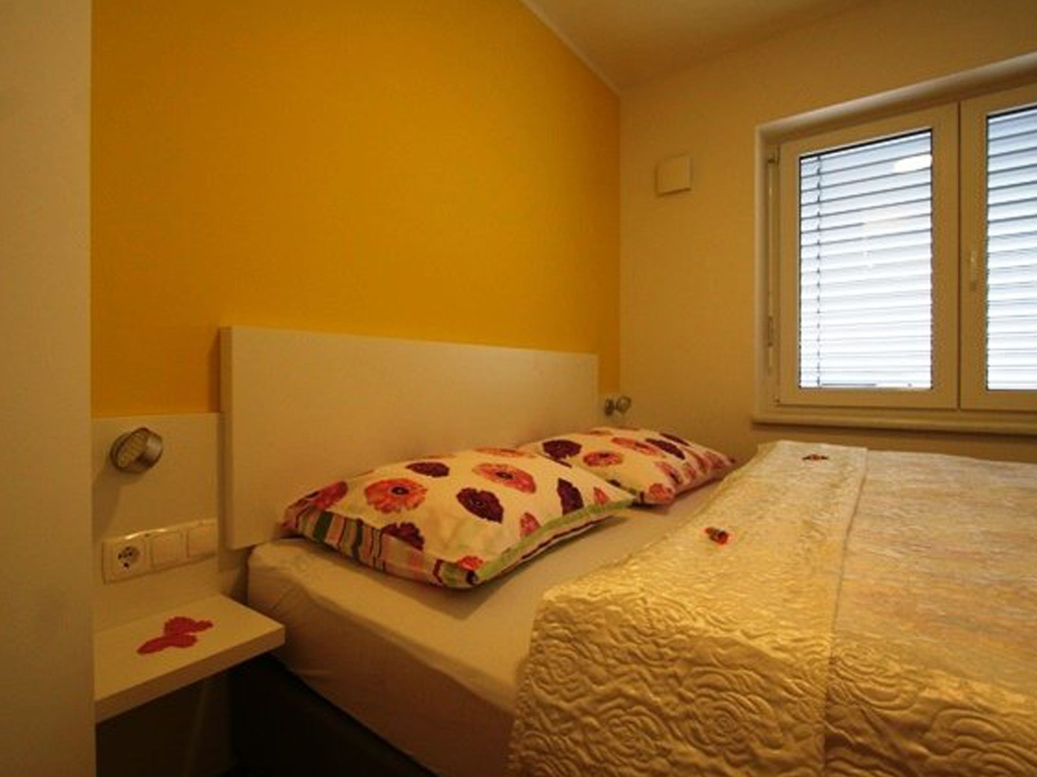A bedroom with a bed, a nightstand, and a window with blinds.