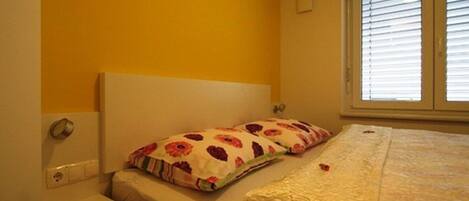 Un dormitorio con cama, mesita de noche y ventana con persianas.