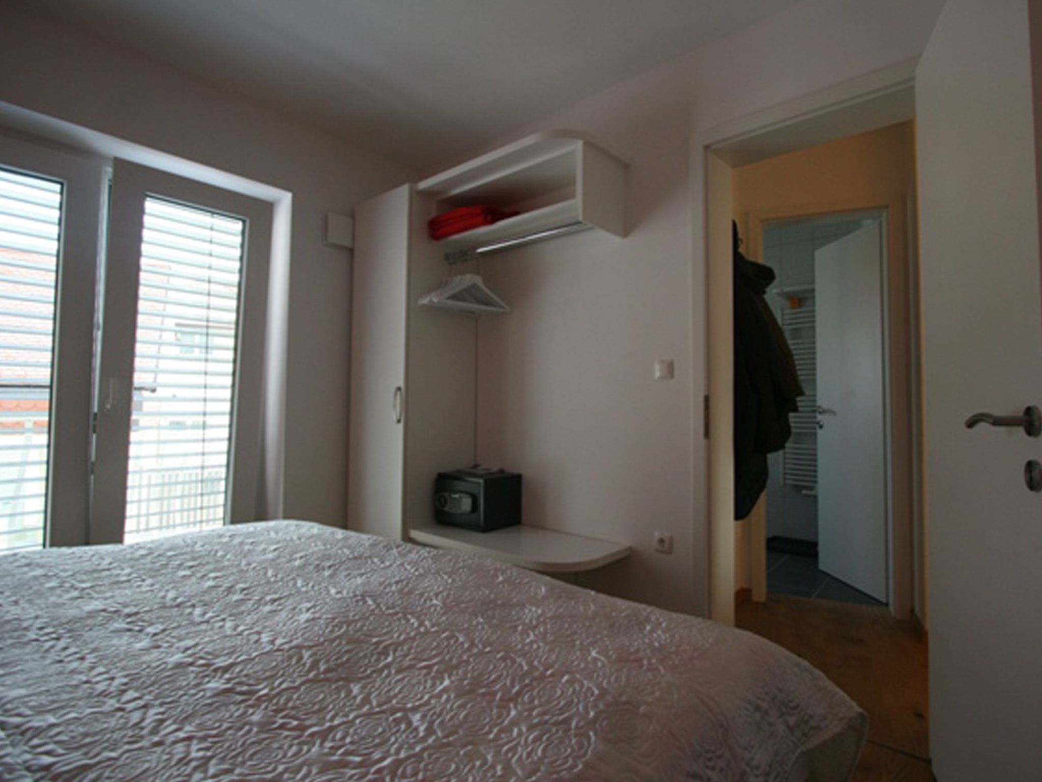 A bedroom with a bed, a built-in shelf with a radio, and a door leading to a hallway.