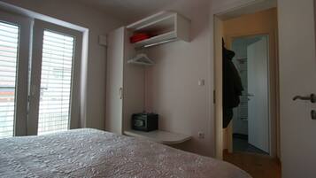 A bedroom with a bed, a built-in shelf with a radio, and a door leading to a hallway.