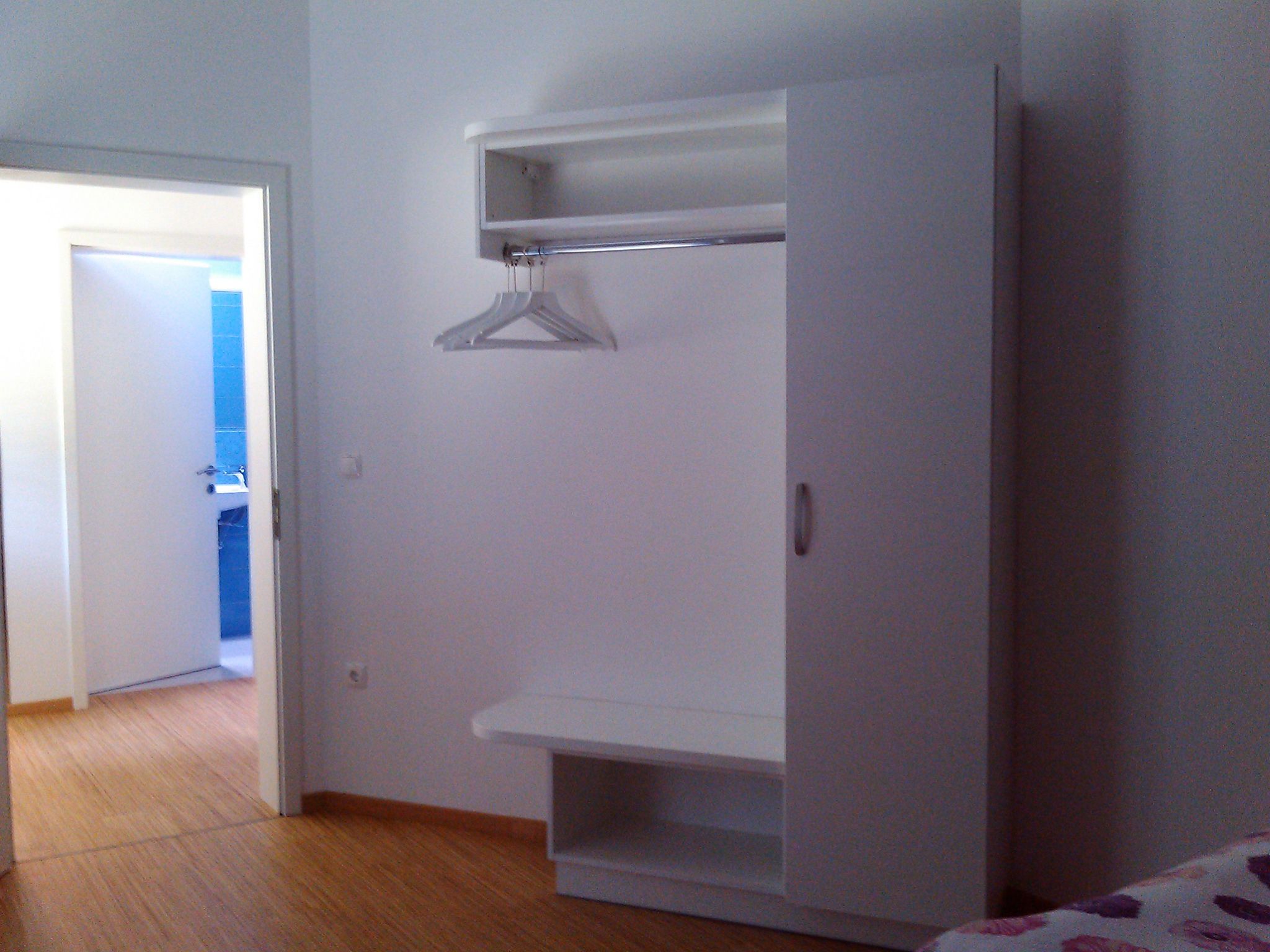 Habitació amb un armari blanc, una porta que dona a un bany i un sòl de fusta.