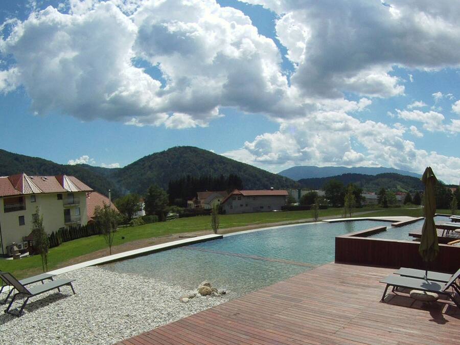 Zona de piscina con sillones de descanso, terraza de madera y vistas a montañas.