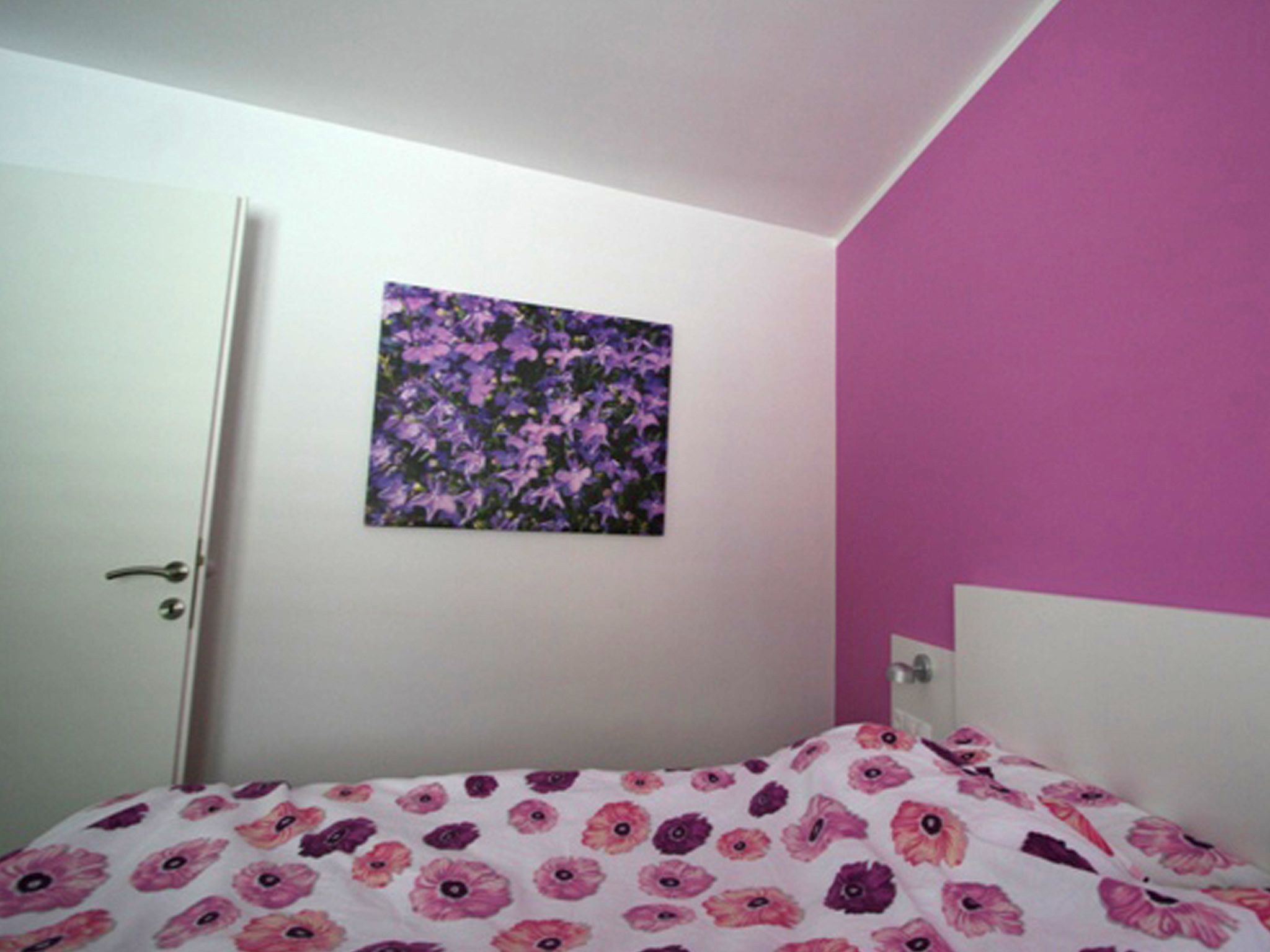 A bedroom with a bed, a door, and a wall with a floral painting.