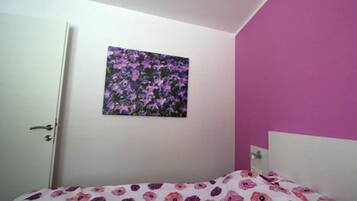 A bedroom with a bed, a door, and a wall with a floral painting.