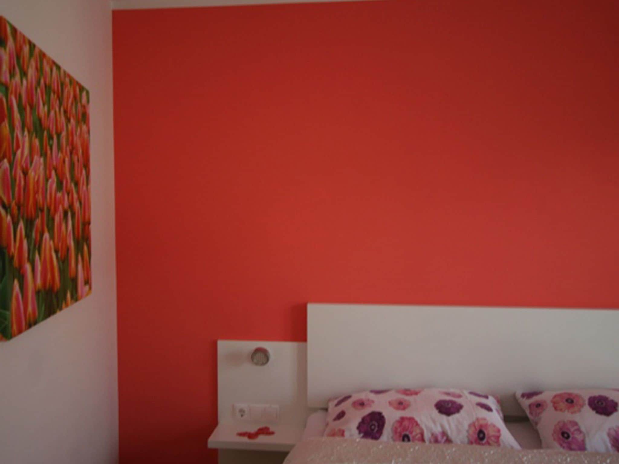 A bedroom with a red wall, a white headboard, and floral-patterned bedding.