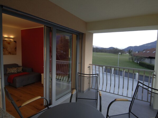 A balcony with a table and chairs, a sofa, and a large sliding glass door leading to a grassy area with a view of hills.