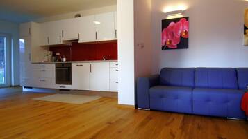 A modern kitchen with white cabinets and a red backsplash, a blue sofa, and a wooden floor.