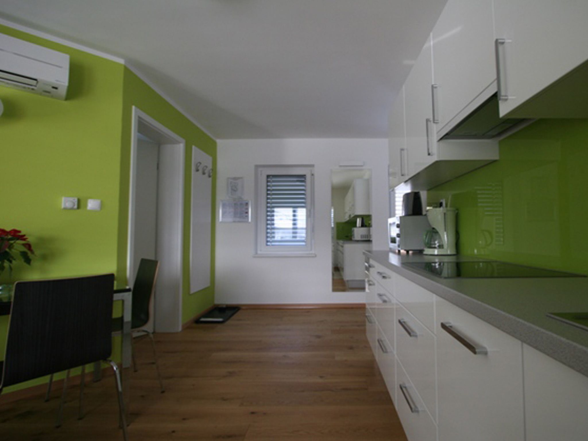A modern kitchen with white cabinets, a green accent wall, and a wooden floor.