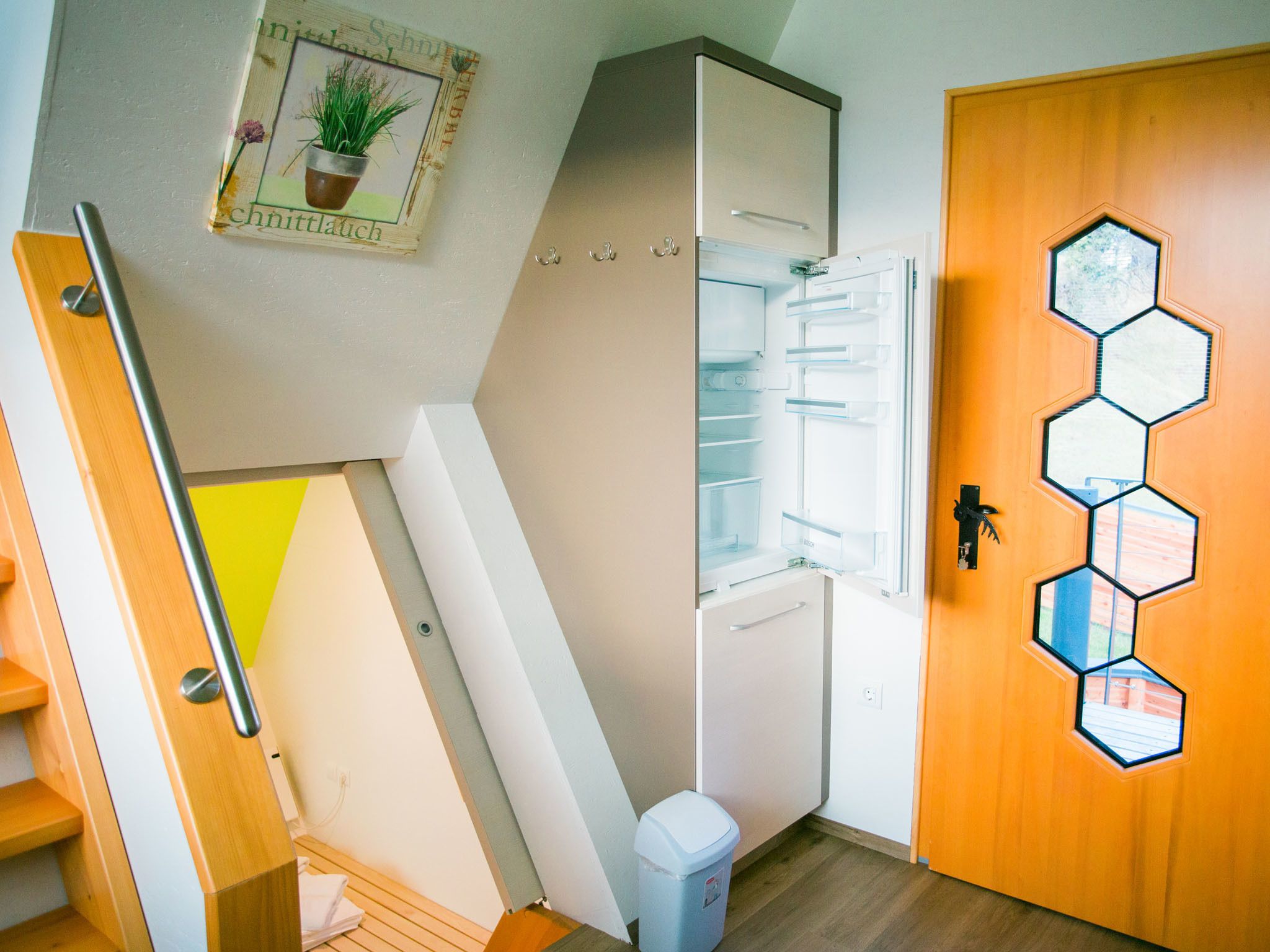 Una cocina moderna con refrigerador empotrado, una puerta de madera con ventanas hexagonales y un pequeño bote de basura.