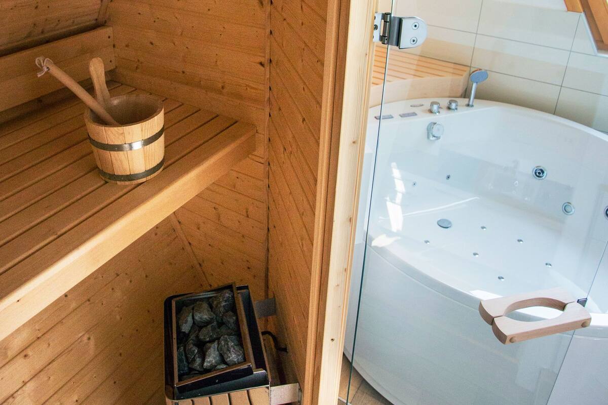 Una sauna de madera con una cuenca de piedra, un balde de madera y un jacuzzi con paredes de vidrio.