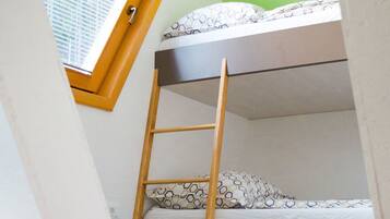 A bunk bed with a wooden ladder, a window with blinds, and patterned bedding.