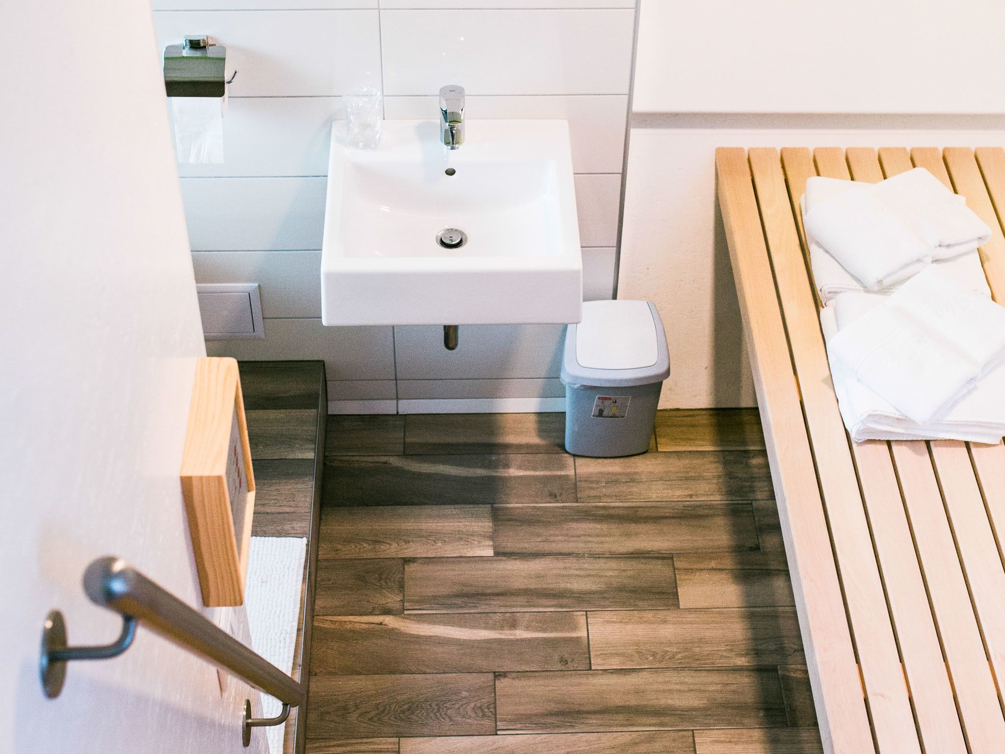 Ein Badezimmer mit Waschbecken, Toilette und einer hölzernen Sitzbank mit Handtüchern.