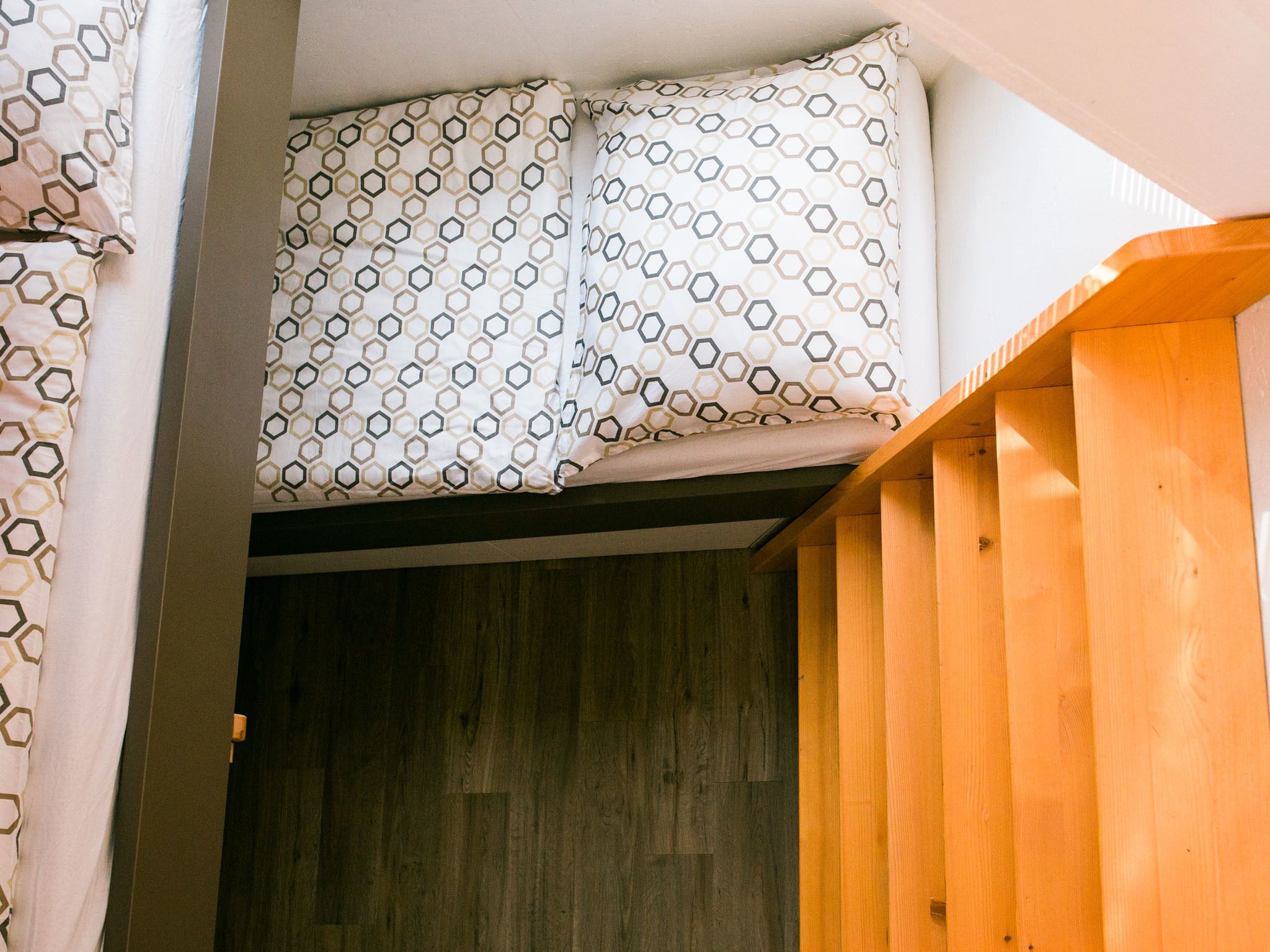 A room with a bunk bed, wooden flooring, and a patterned curtain.