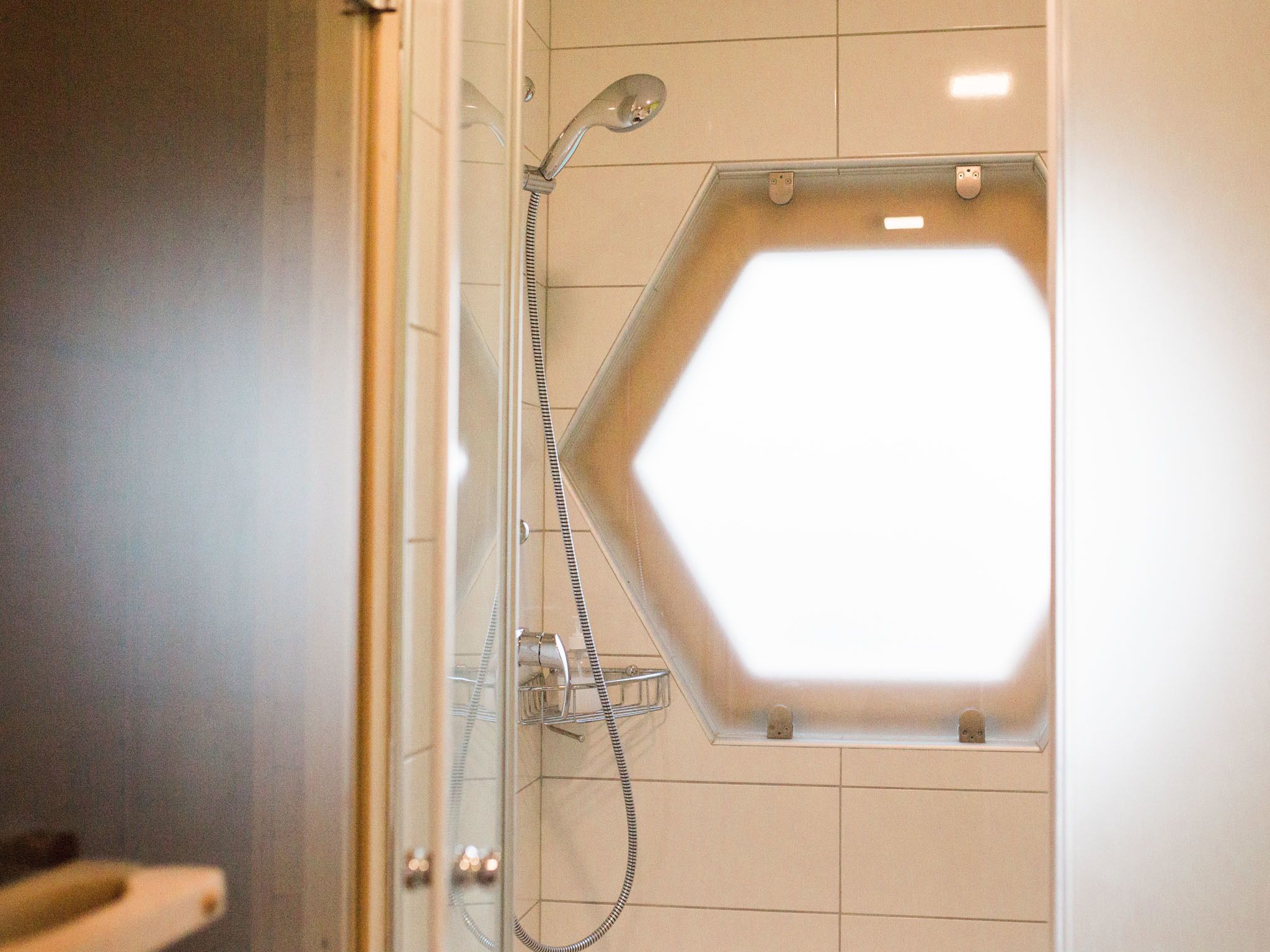 A shower with a hexagonal window, a handheld showerhead, and a wall-mounted faucet.