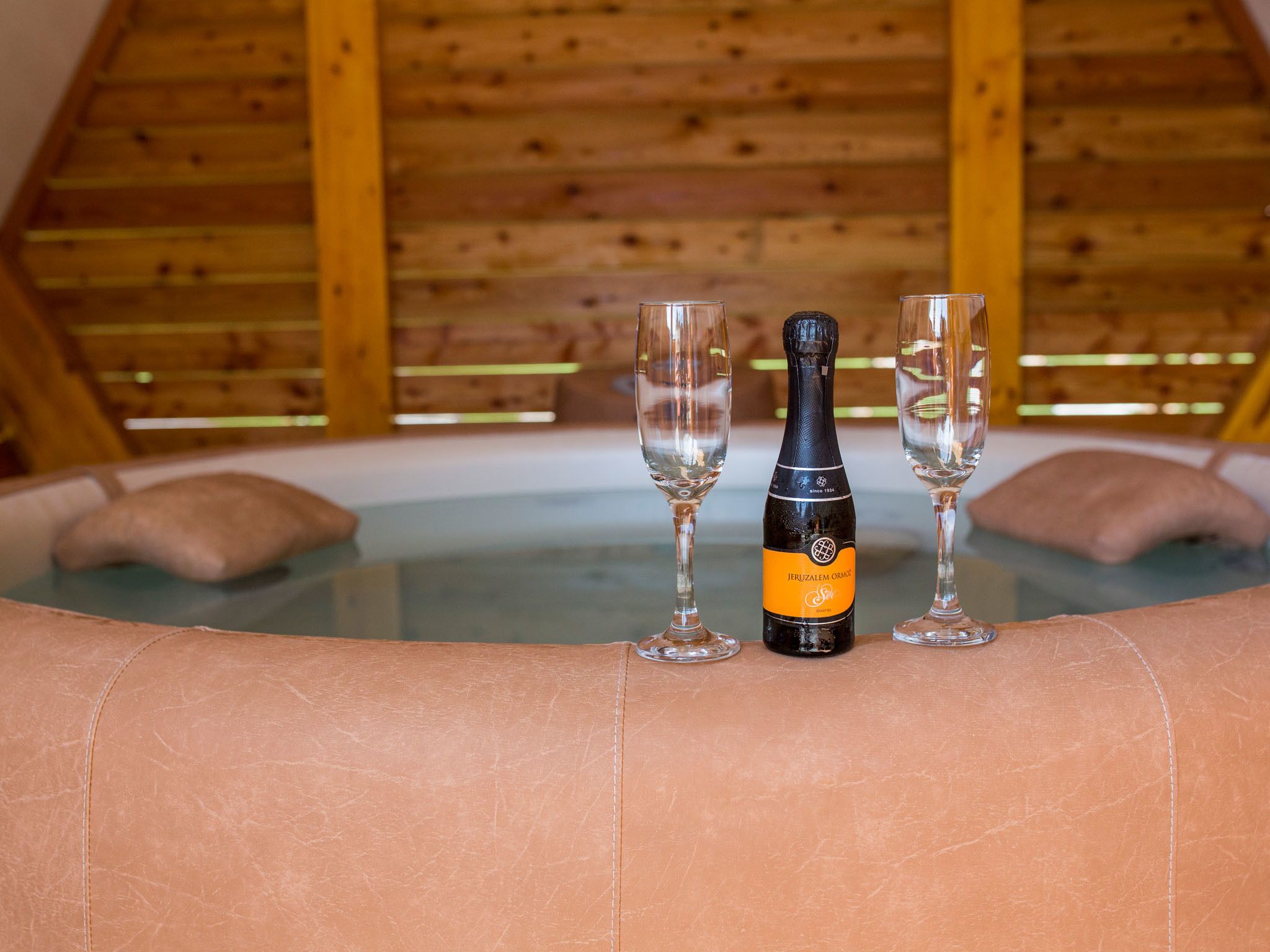 A hot tub with two glasses and a bottle of champagne in a wooden cabin setting.