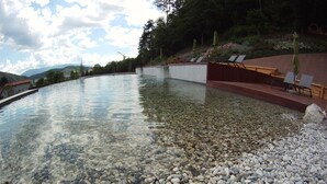 Una piscina cristalina con fondo de piedrecitas, rodeada por una terraza de madera y sillones de descanso.