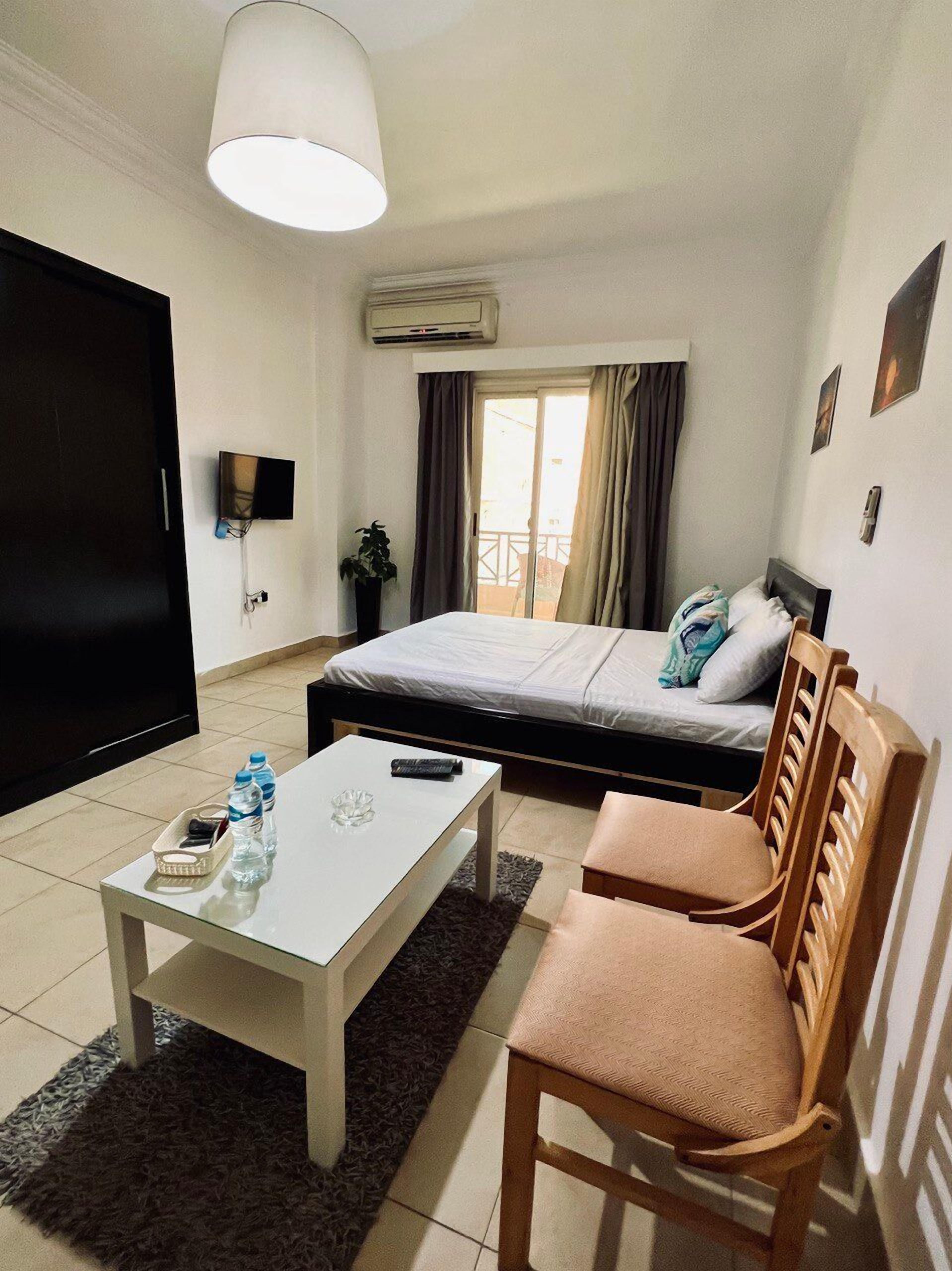 A small, well-lit room with a bed, a TV, a table, and two chairs.