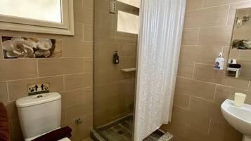 Ein Badezimmer mit Dusche, Toilette, Waschbecken und einem Fenster.