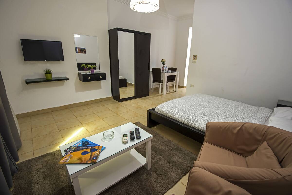 A modern bedroom with a bed, a TV, a desk, and a mirror.