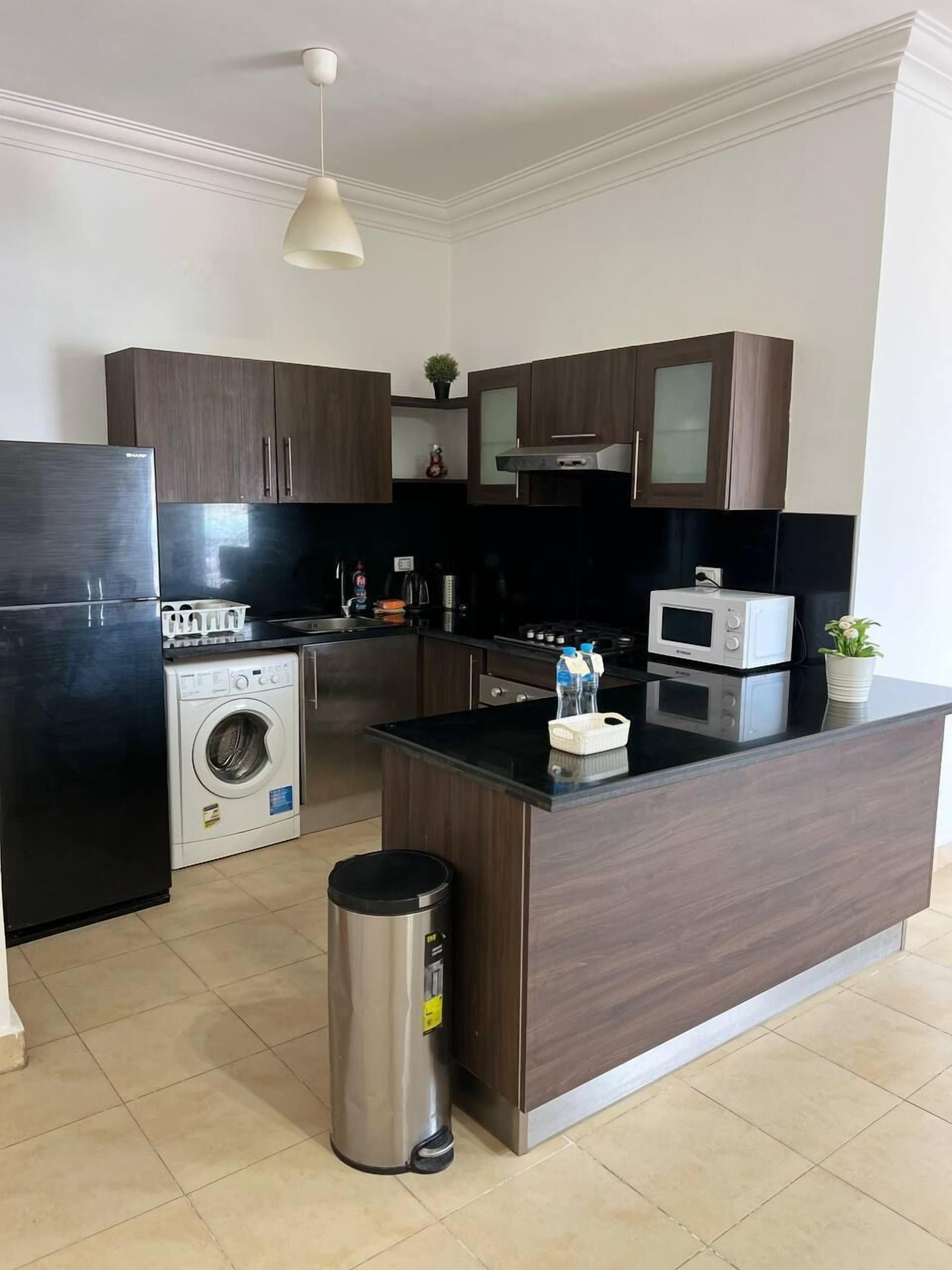 A modern kitchen with dark wooden cabinets, stainless steel appliances, a built-in washing machine, and a central island with a sink.