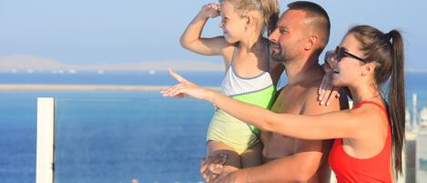 A family of three on a balcony overlooking a coastal view.