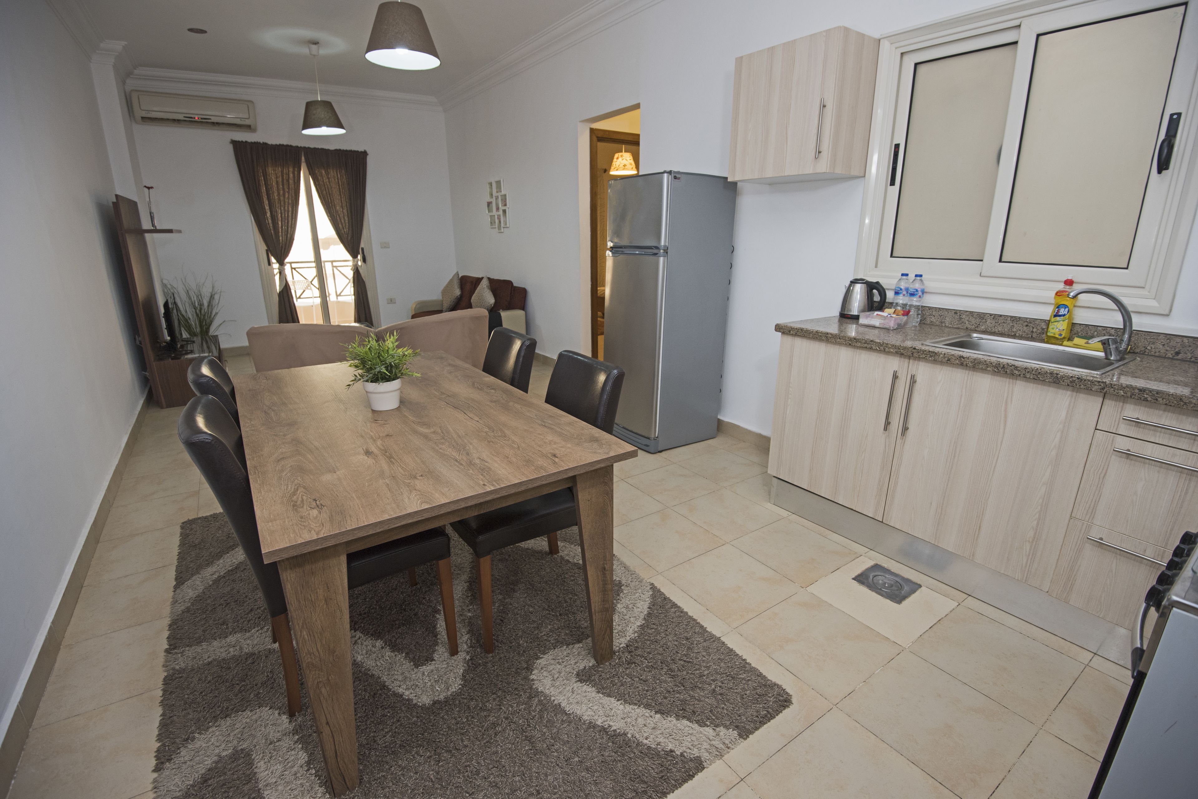 A modern kitchen with a built-in refrigerator, a dining area with a wooden table and chairs, and a small countertop with a sink and cabinets.