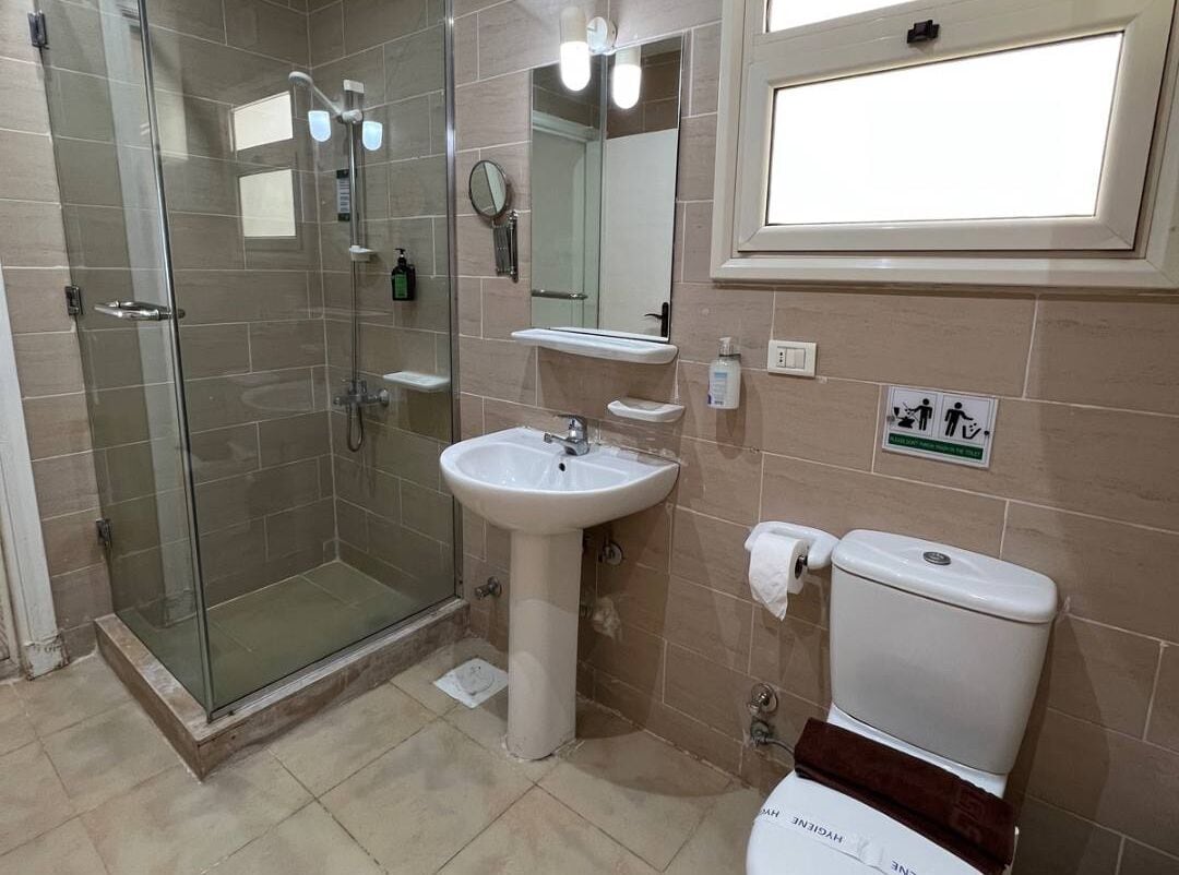 Une salle de bain avec une douche à parois de verre, un lavabo sur colonne, des toilettes et un miroir.