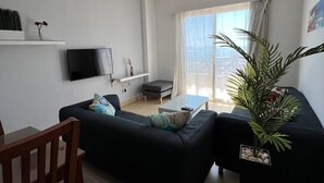 A modern living room with a black sofa, a wooden chair, a coffee table, and a potted plant.