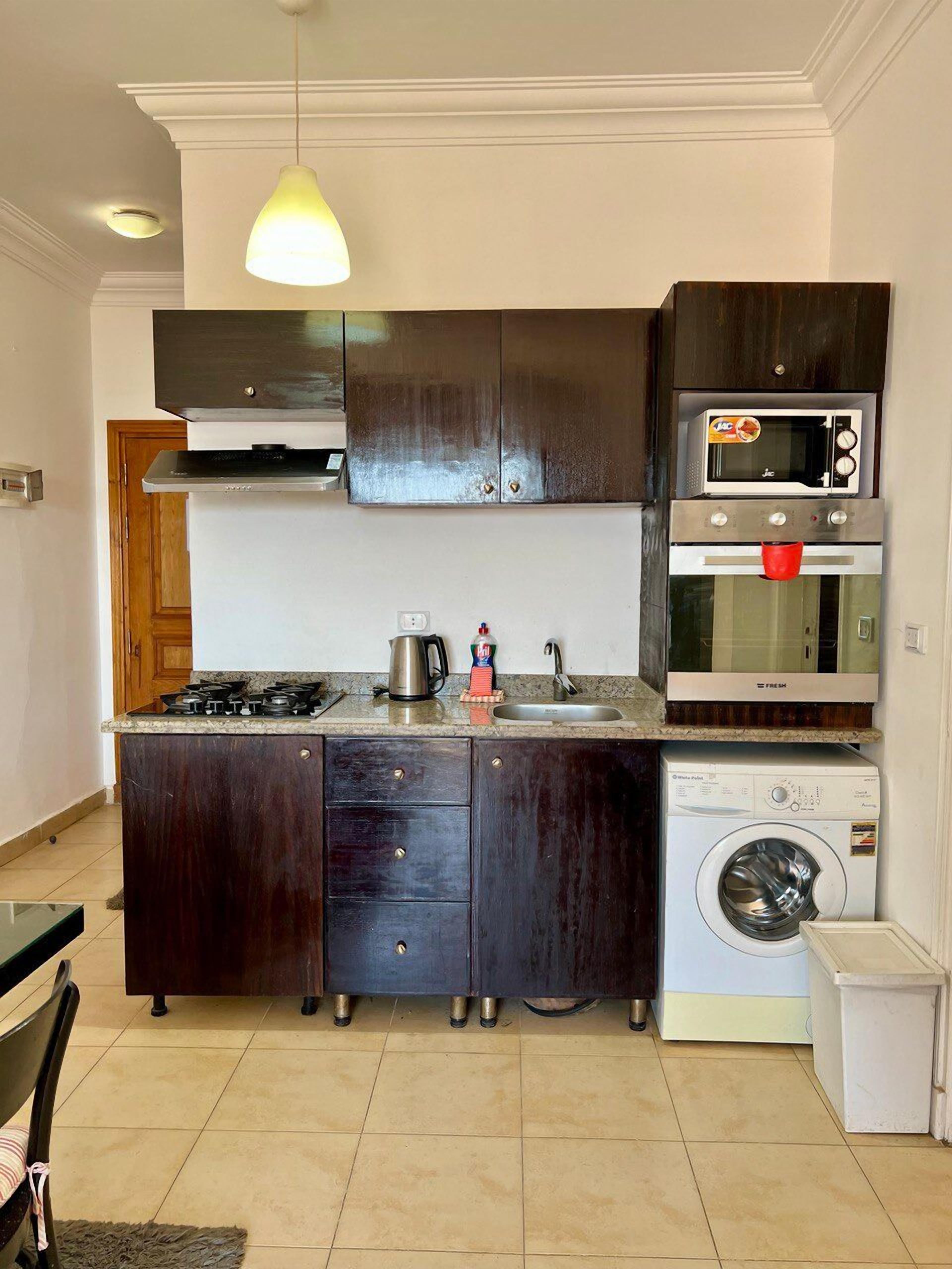 A compact kitchen with dark cabinets, a gas stove, a microwave, an oven, and a washing machine.