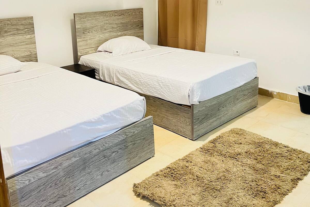 A hotel room with two beds, a wooden headboard, a beige rug, and an air conditioning unit.