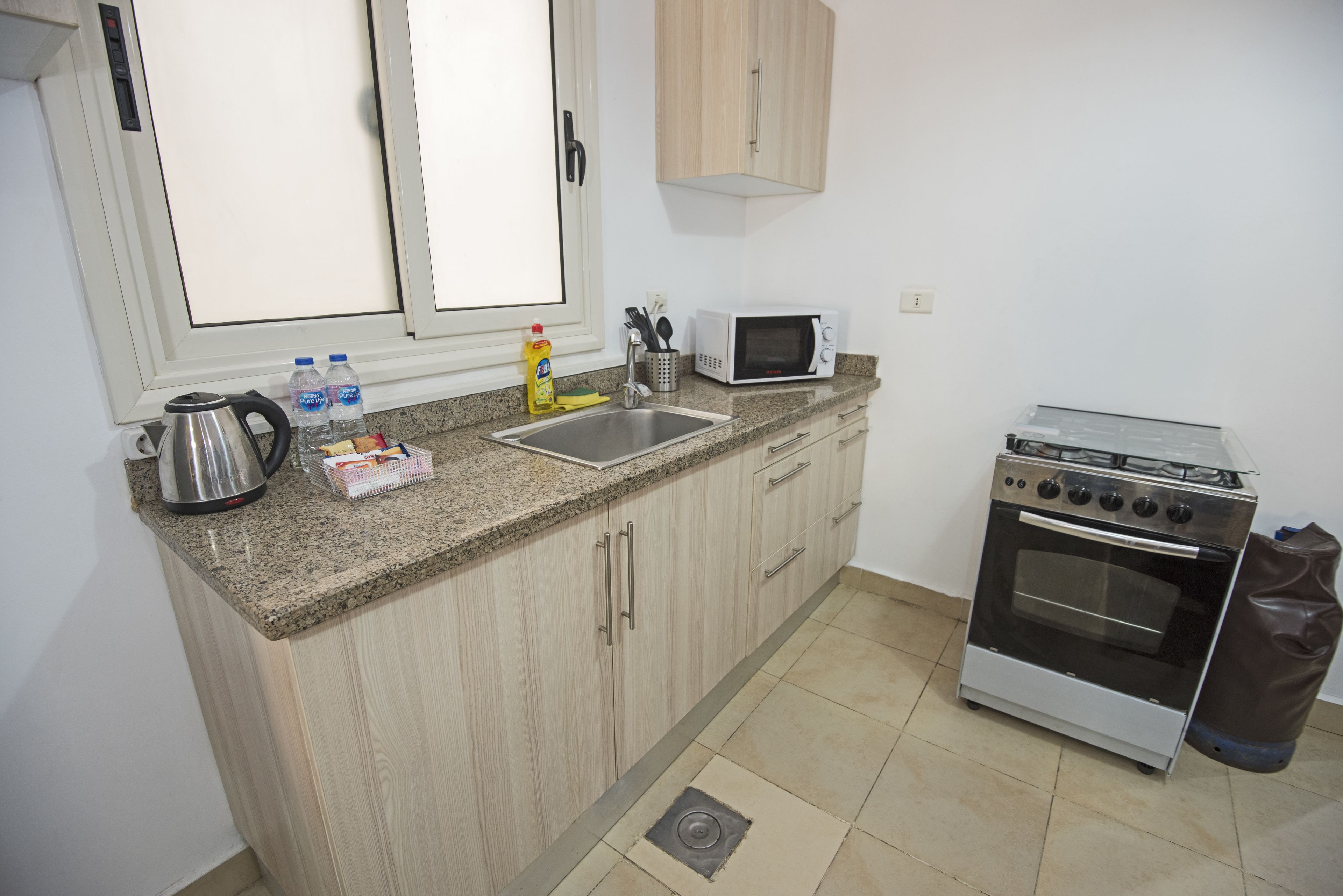Una cocina compacta con encimera de granito, hervidor de acero inoxidable, microondas y estufa a gas.