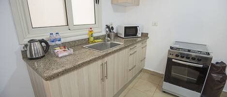 Una cocina compacta con encimera de granito, hervidor de acero inoxidable, microondas y estufa a gas.