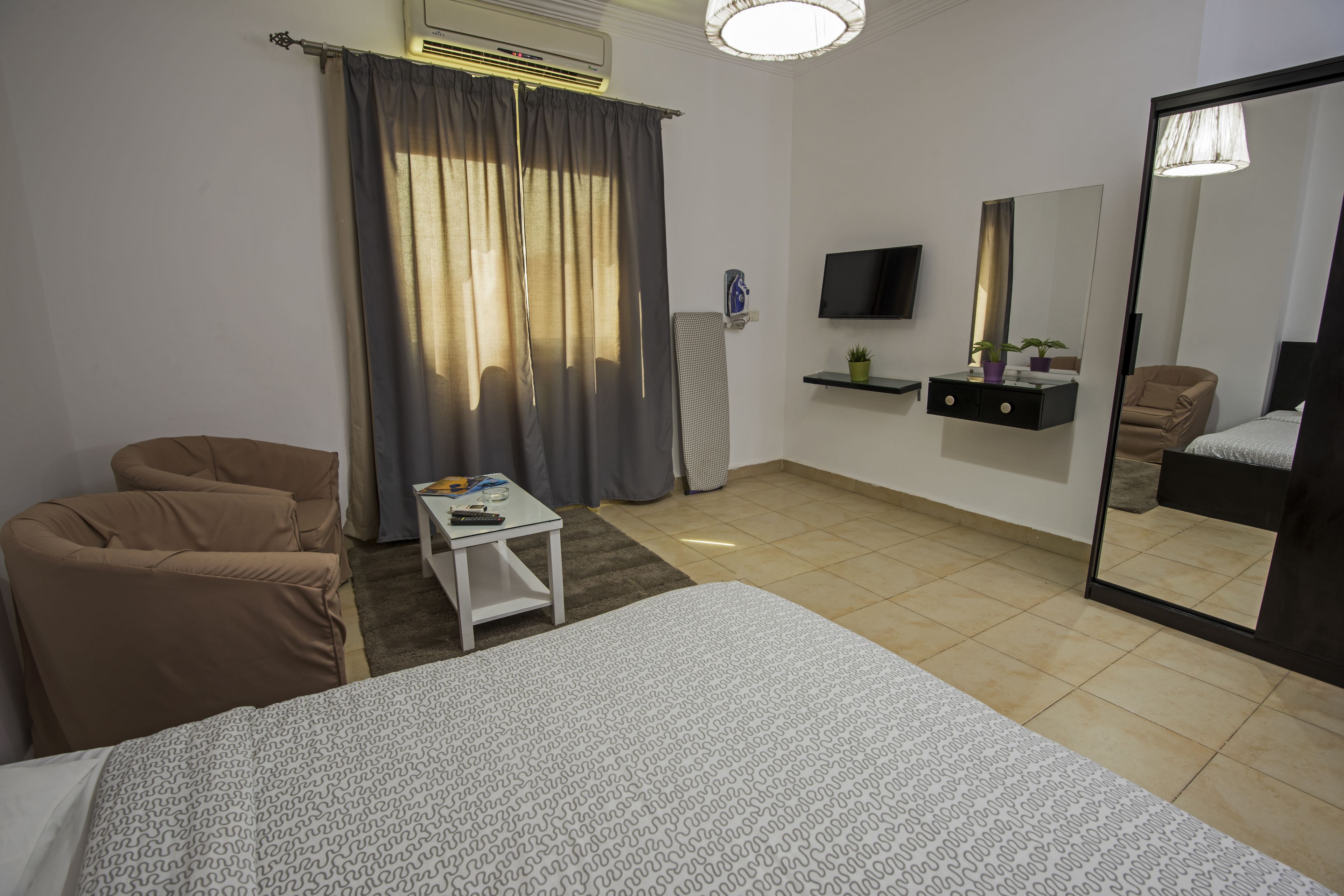 A hotel room with a bed, a sofa, a small table, a TV, a mirror, and a window with curtains.