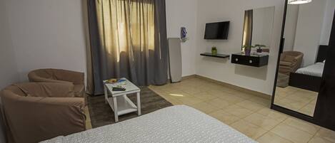 A hotel room with a bed, a sofa, a small table, a TV, a mirror, and a window with curtains.