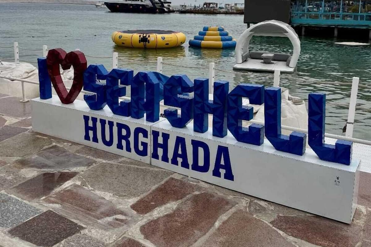 A sign with 'Heart of the Sea' and 'HURGADA' text, a dock with boats, and a calm sea.