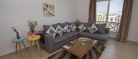 Una sala de estar con un sofá gris, una mesa de centro de madera y vistas de la ciudad a través de amplias ventanas.
