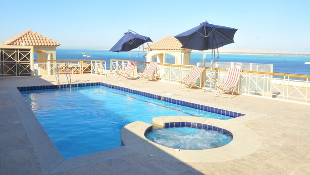 A swimming pool with a hot tub, lounge chairs, and umbrellas.