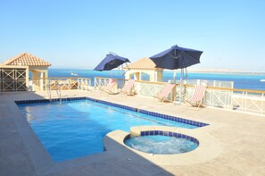 Ein Pool mit Whirlpool, Liegestühlen und Sonnenschirmen.