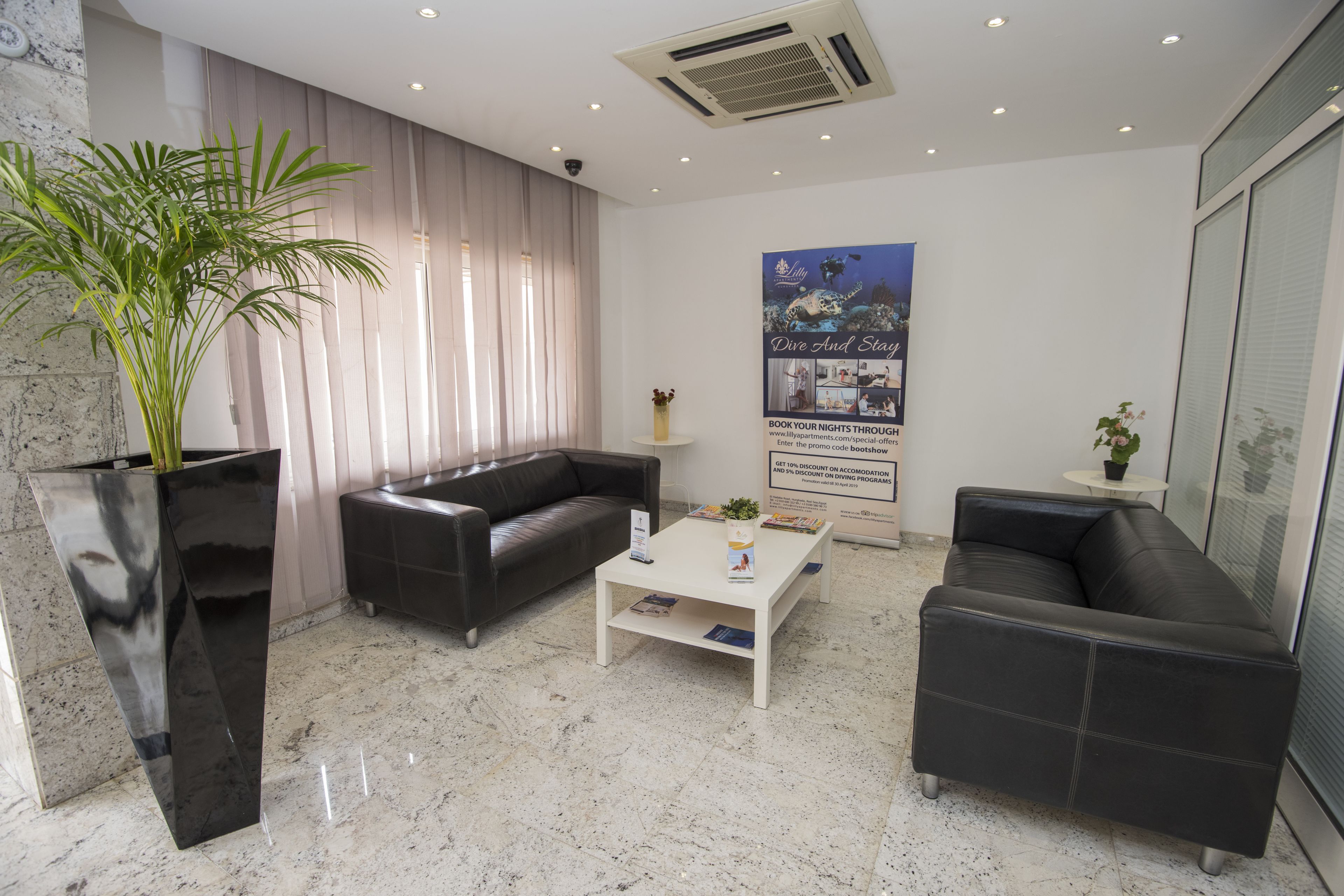 Un vestíbulo moderno con piso de mármol, sofás de cuero negro, una mesa de centro blanca y un cartel grande que anuncia un espectáculo de buceo y escenario.