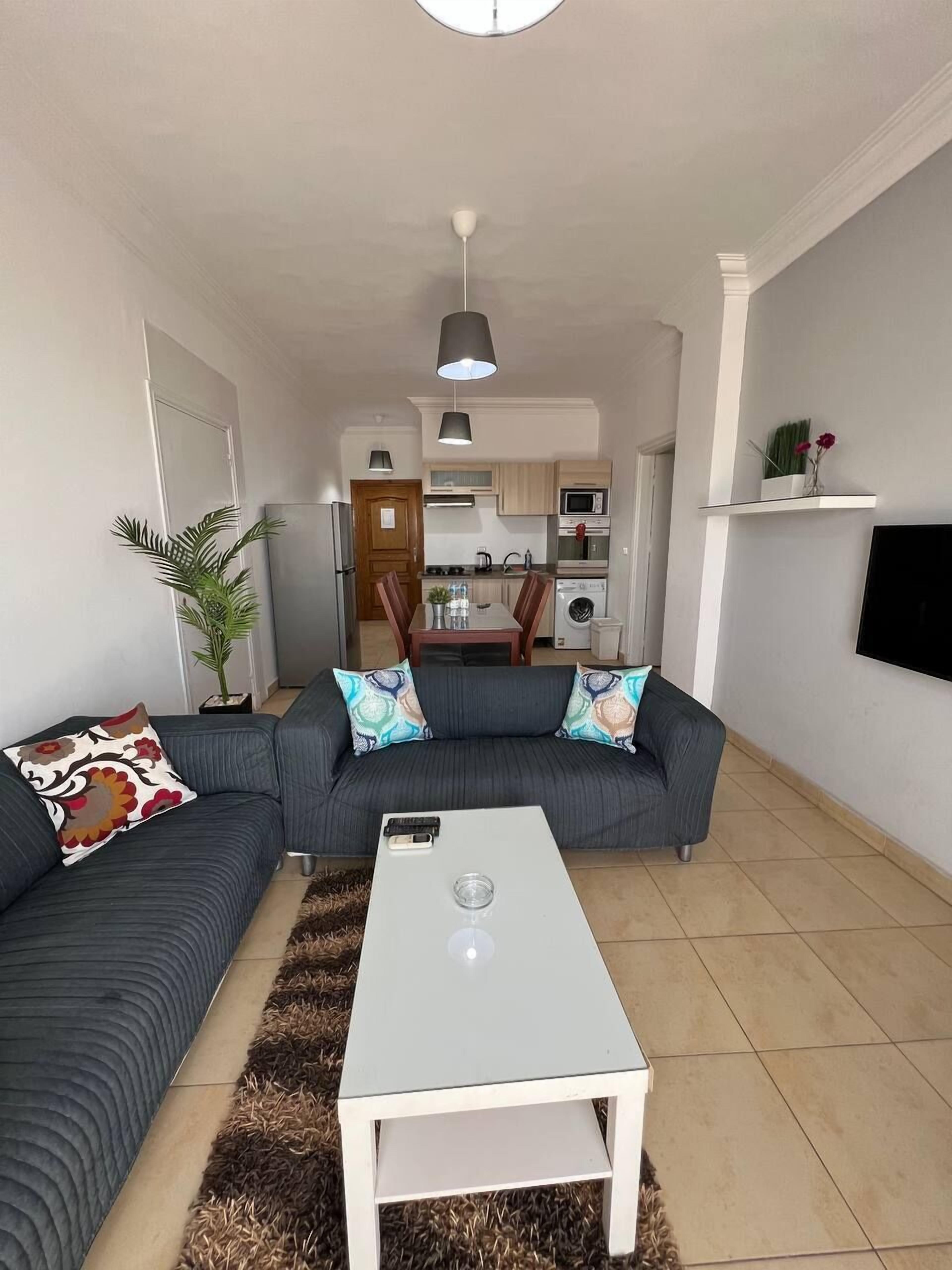 A modern living room with a sofa set, a coffee table, and a kitchen in the background.