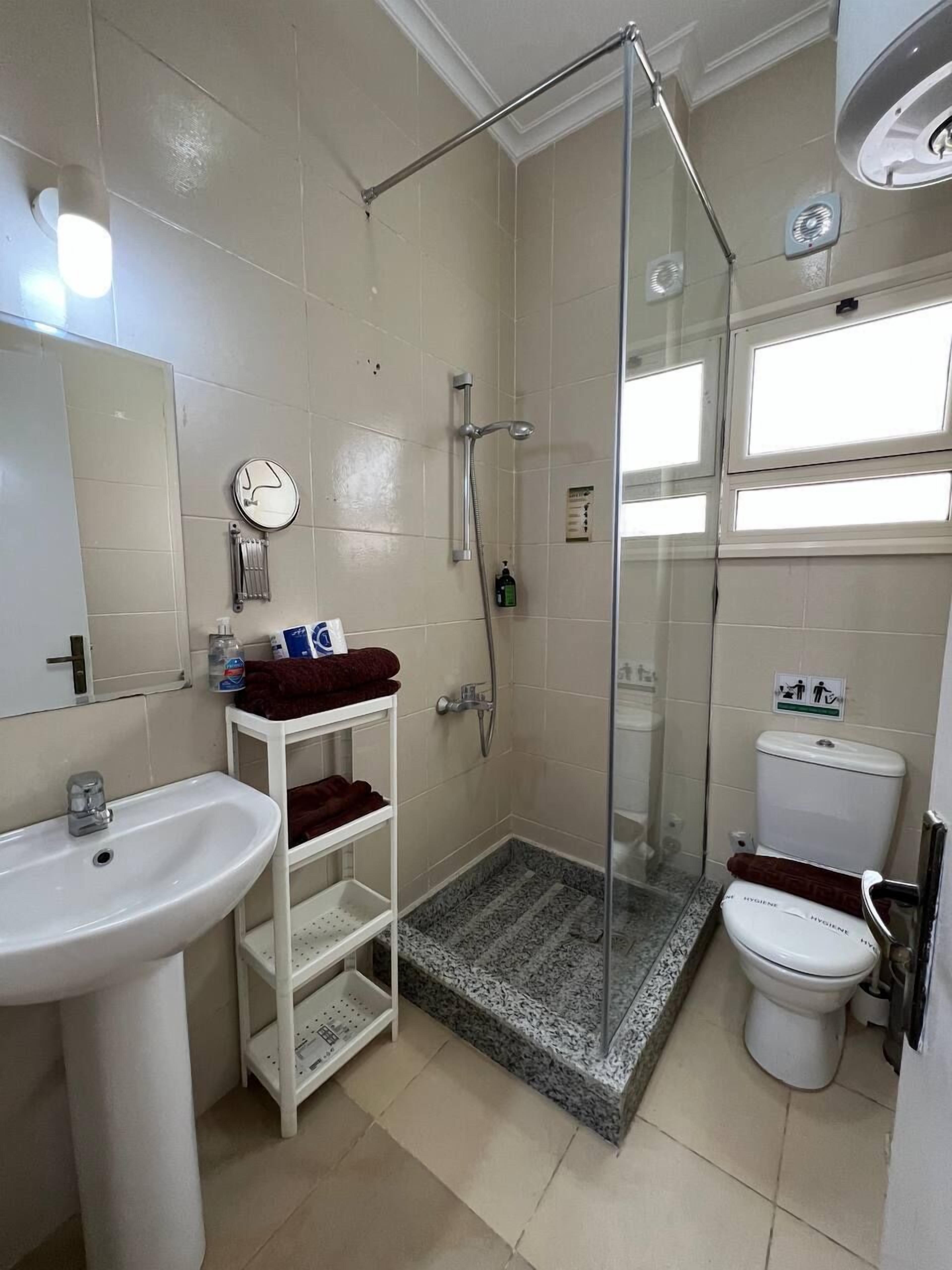 Un baño con ducha de vidrio, lavamanos, inodoro y repisa con toallas.